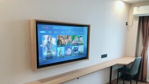 Un salon moderne doté d’un téléviseur fixé au mur qui diffuse différents programmes, d’un banc en bois, d’une chaise et d’un appareil de climatisation fixé au plafond.