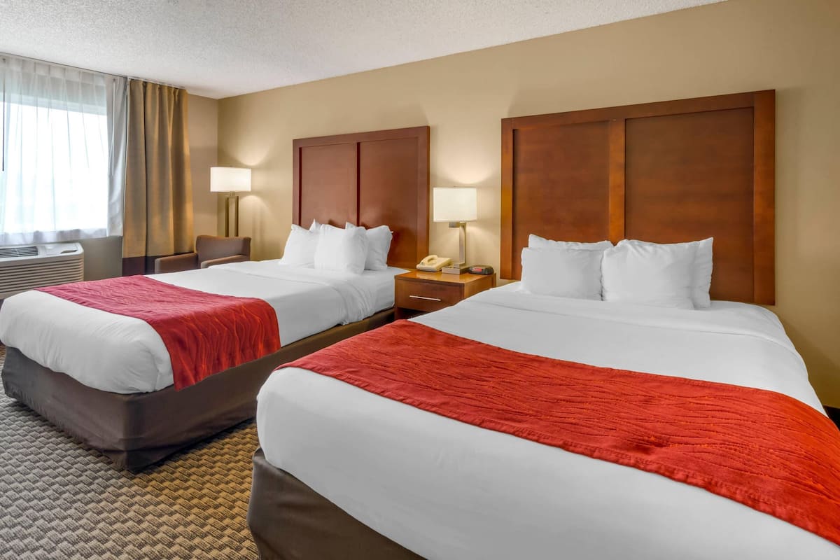 A hotel room with two beds, each with a red and white bedspread, a wooden headboard, bedside lamps, and a small table with a telephone.