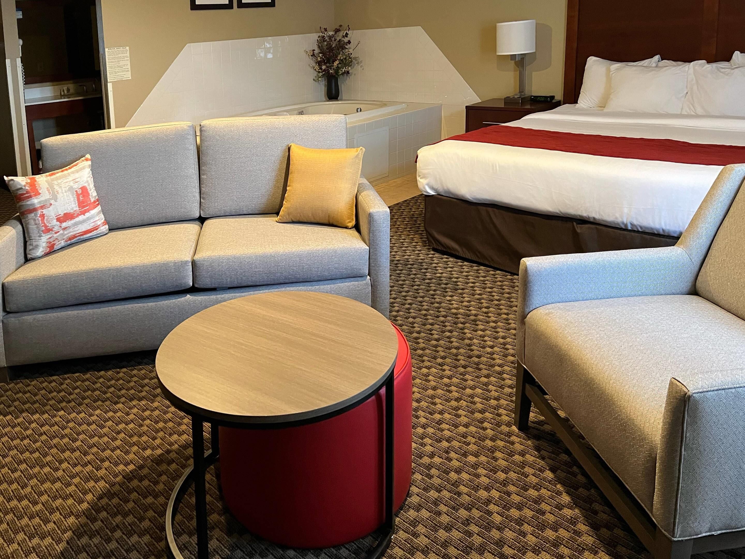 Une chambre d’hôtel comprenant un canapé, un fauteuil, une table ronde, un lit et une petite table avec une lampe.