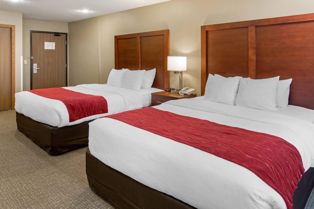 A hotel room with two beds, a wooden headboard, a nightstand with a lamp, and a door with a sign.