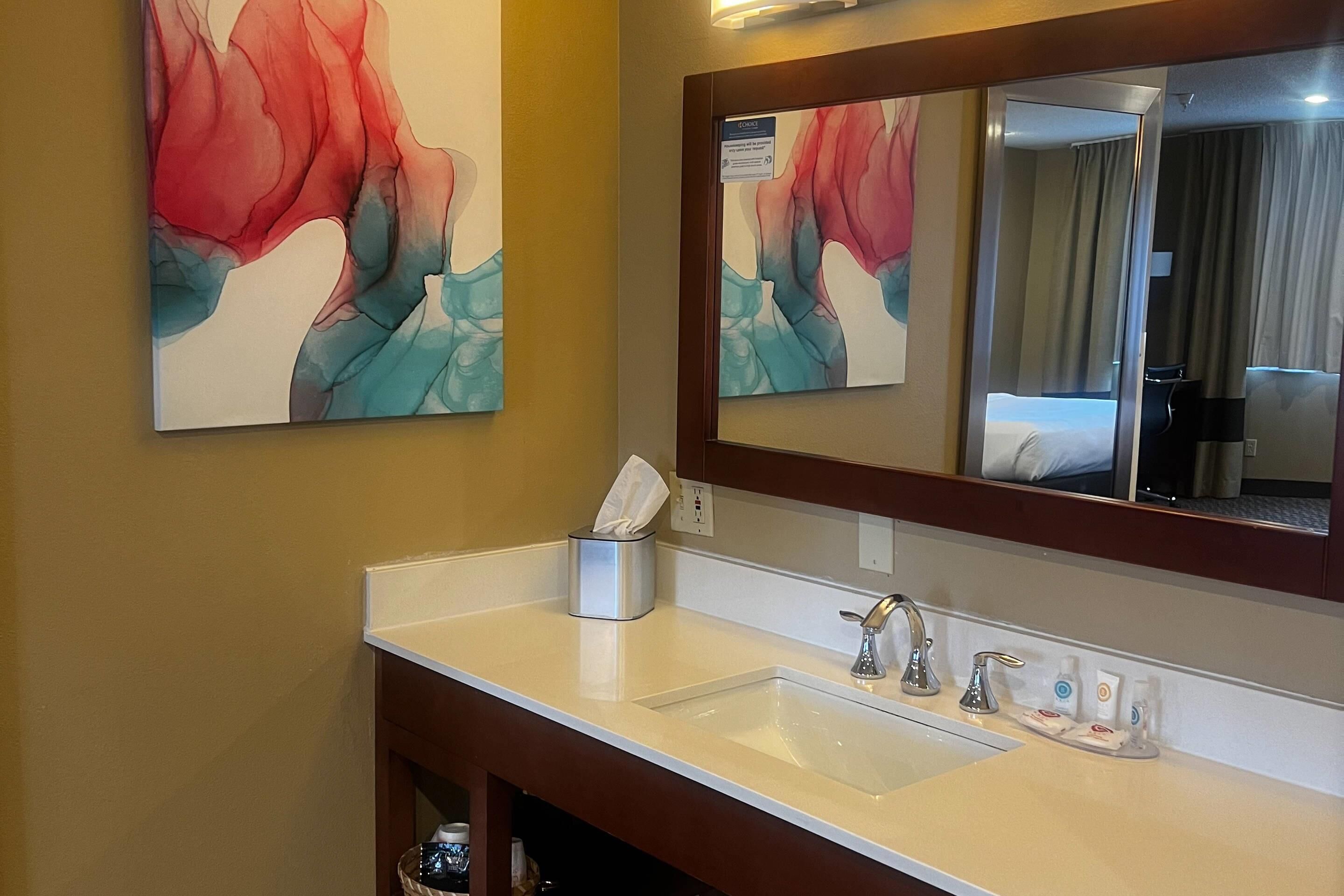 A hotel bathroom with a white sink, a mirror, and two abstract paintings on the wall.