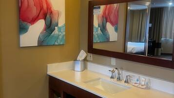 A hotel bathroom with a white sink, a mirror, and two abstract paintings on the wall.