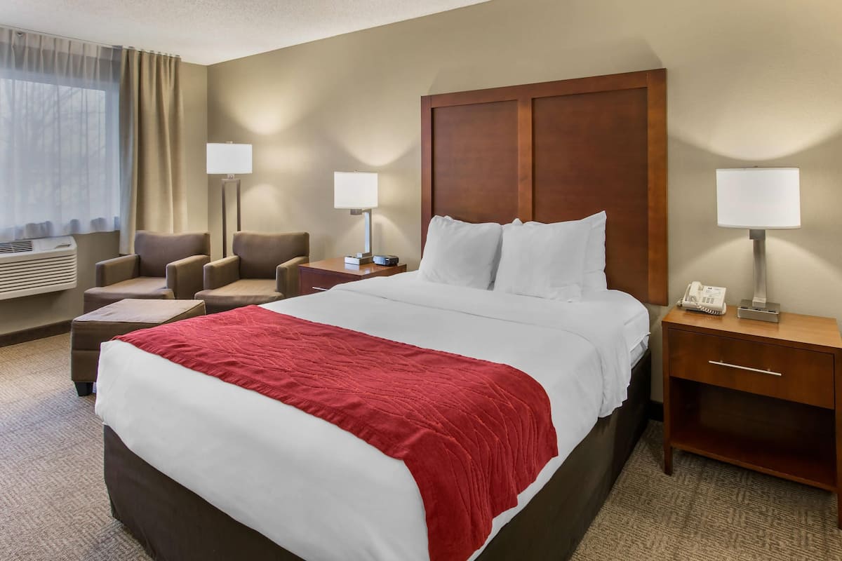 A hotel room with a large bed, two bedside tables with lamps, a chair, and a desk.