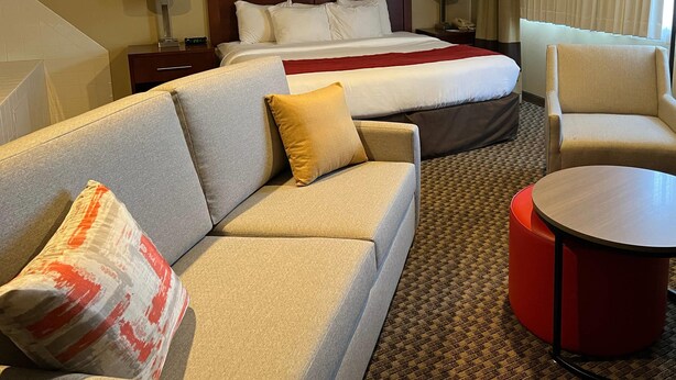 Una habitación de hotel con una cama, un sofá, un reposapiés rojo y una pequeña mesa redonda.
