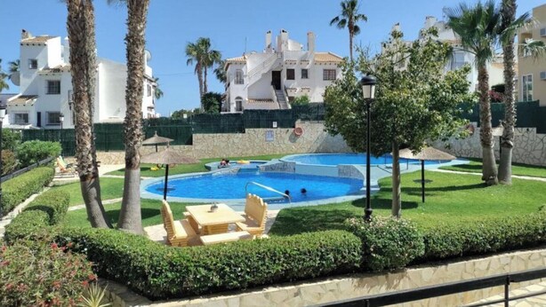 A pool area with lounge chairs, palm trees, and a building in the background. - stunning apartment overlooking the pool (Orihuela)