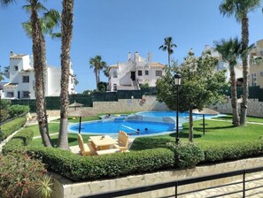 A pool area with lounge chairs, palm trees, and a building in the background. - stunning apartment overlooking the pool (Orihuela)