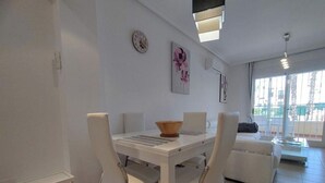 A modern dining area with a white table and chairs, a small trash bin, and a wall clock. - stunning apartment overlooking the pool (Orihuela)