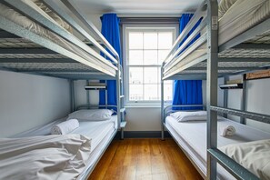 A dormitory room with bunk beds, a window with blue curtains, and a wooden floor. - ST Christopher's INN Oasis - London Bridge - Female Only (London)