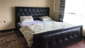 Un dormitorio con cabecera tapizada en negro, ropa de cama con estampado floral y vistas al exterior a través de una ventana con cortinas.