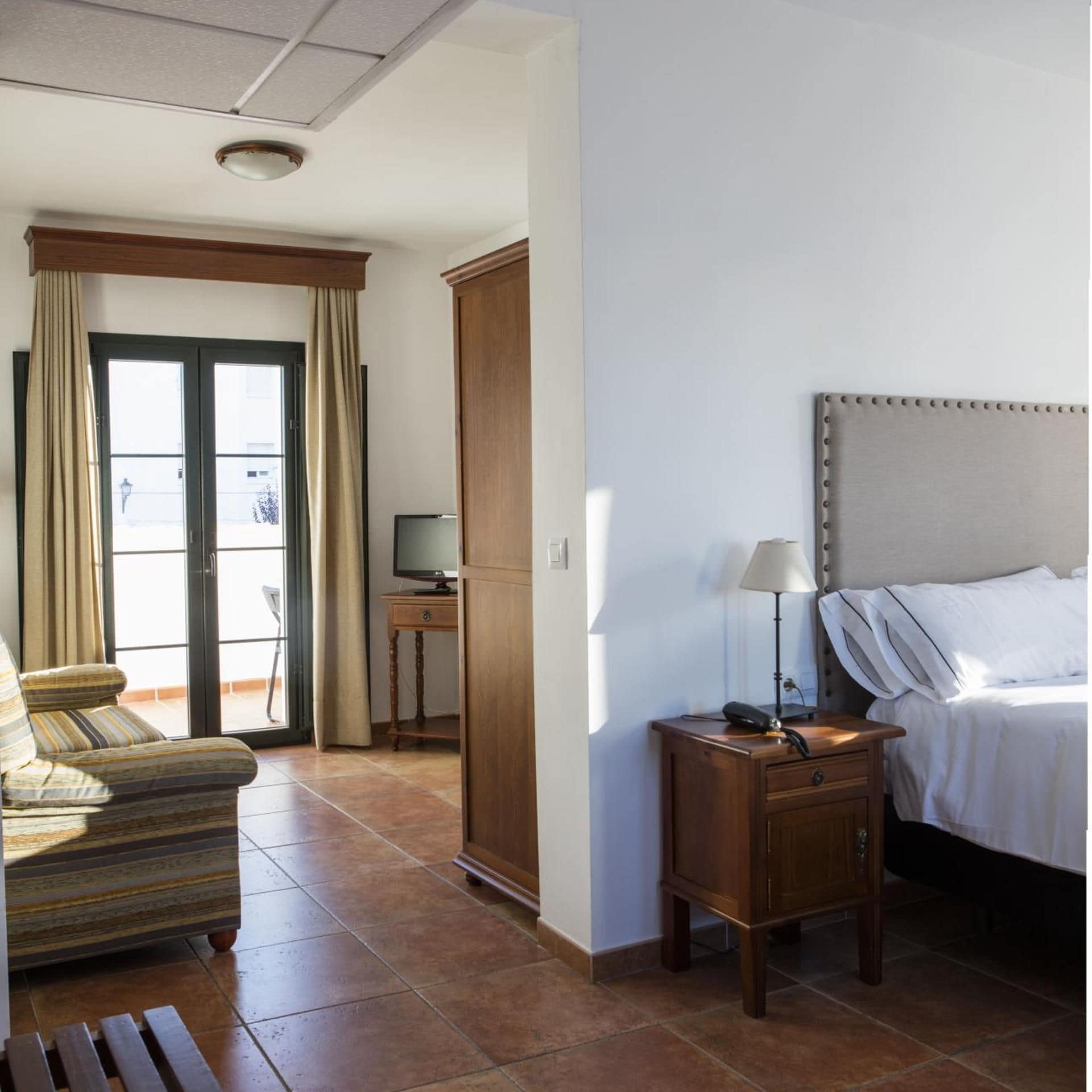Habitación de hotel con cama, escritorio con lámpara, una silla y vista por una puerta.