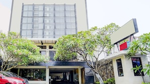 A modern building with a large glass facade, a covered entrance, and a parking area with a red car. - OYO Flagship  90425 Hotel 22 (Surabaya)