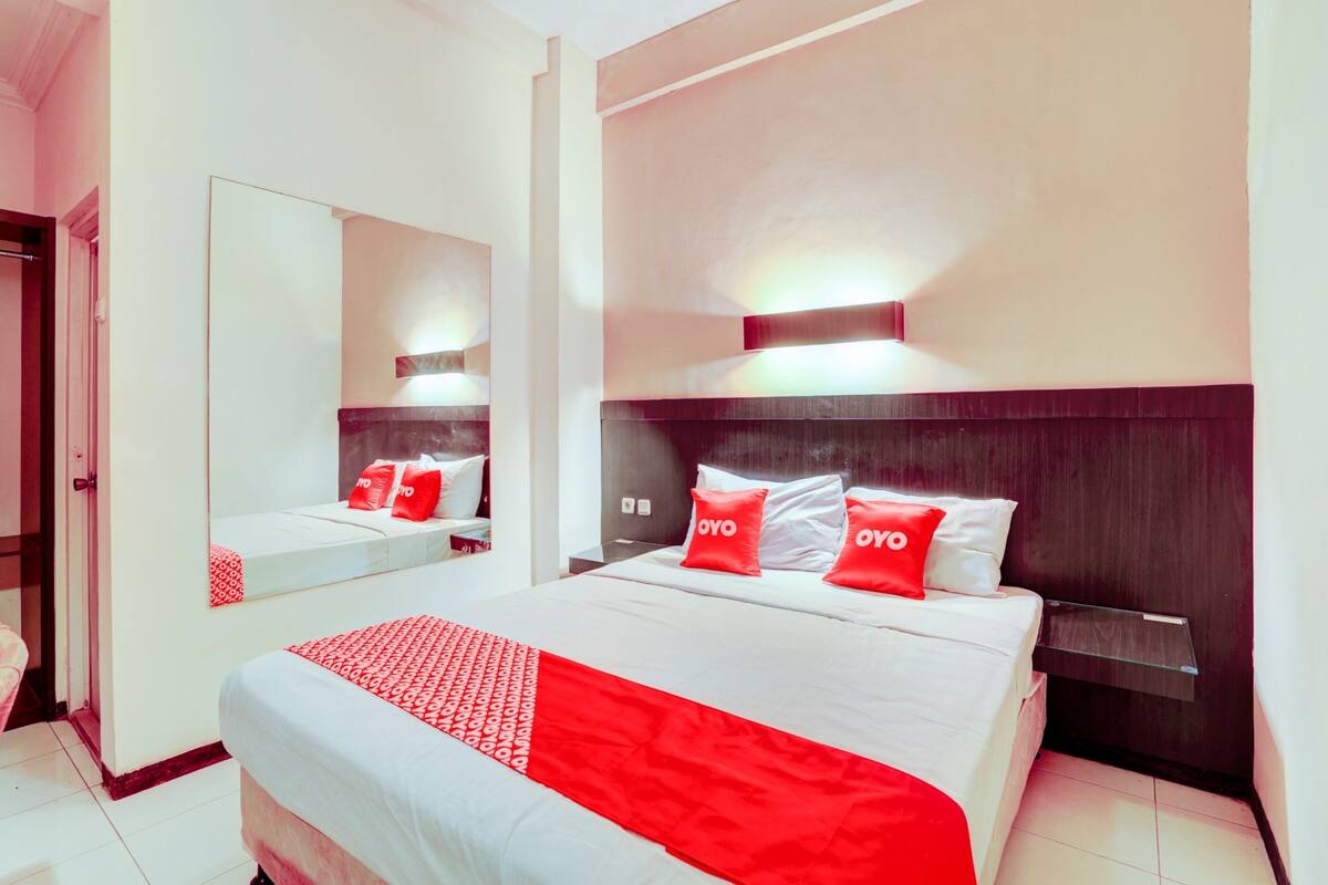 Quarto de hotel com cama grande, mesa de cabeceira, espelho e luminária na parede.