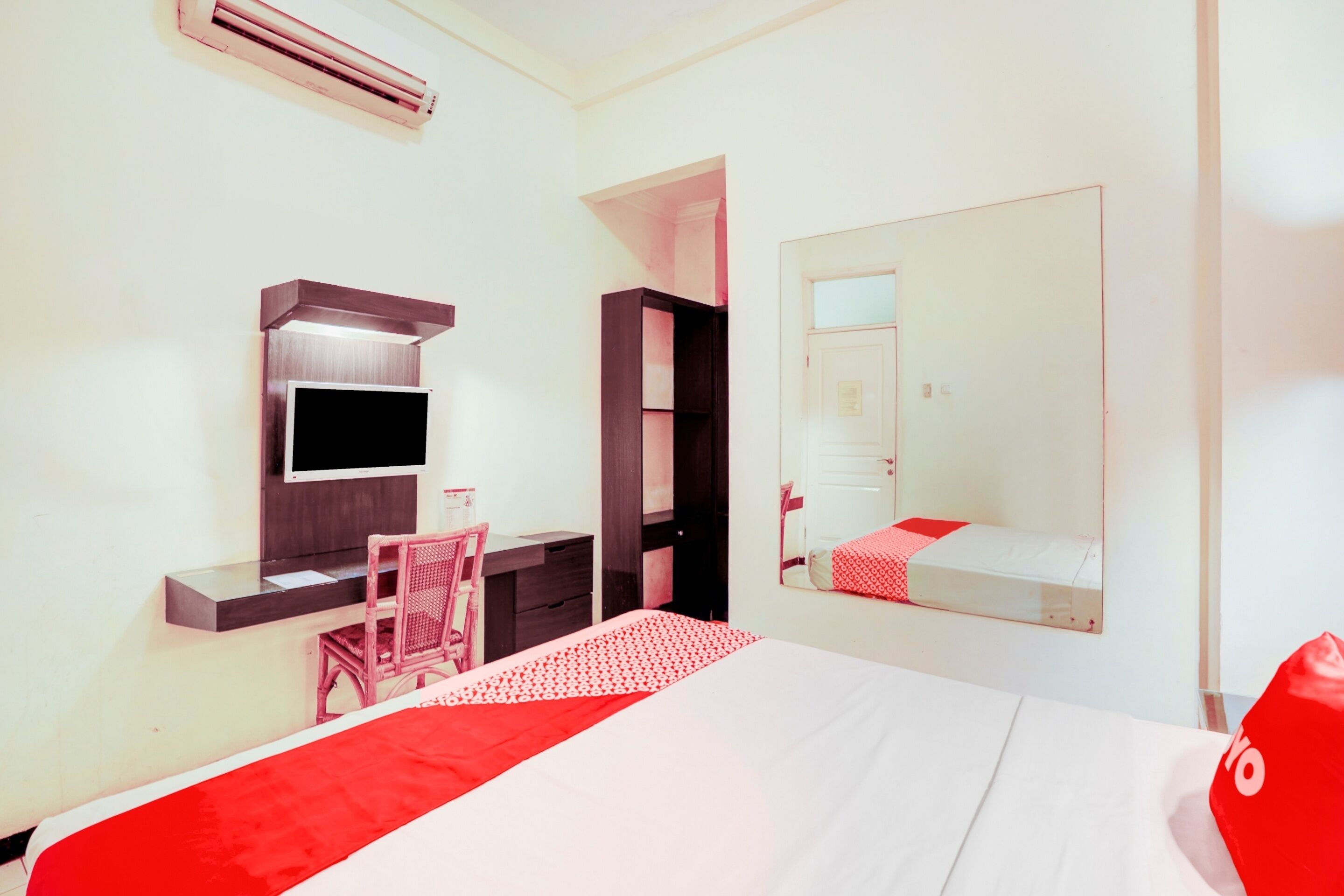 Quarto de hotel com cama, escrivaninha, cadeira, televisão, armário e espelho.