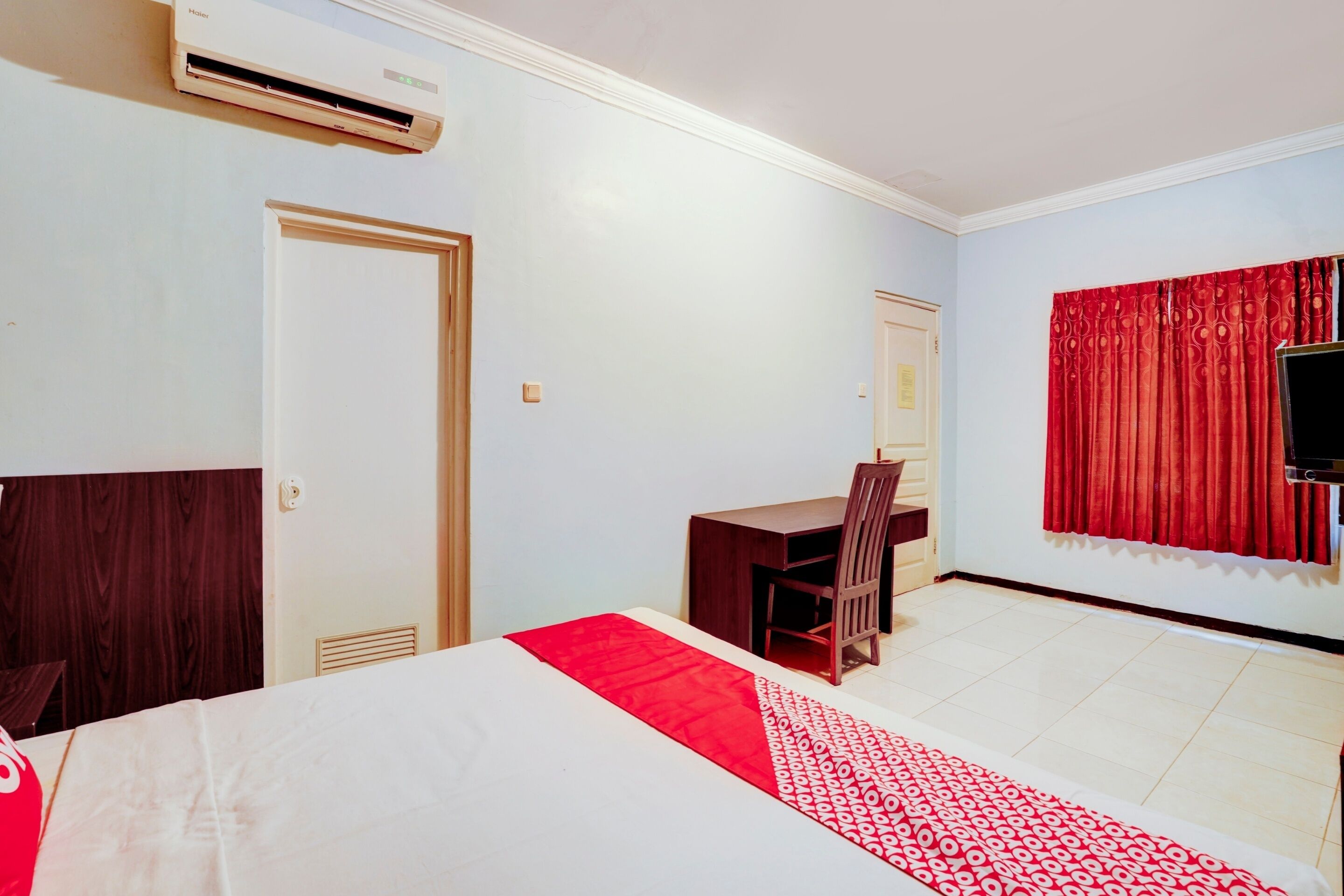 A hotel room with a bed, a desk, a chair, a TV, and a red curtain.