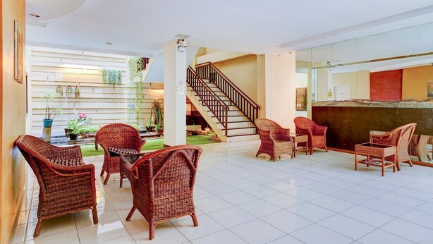 A spacious lobby with wicker furniture, a staircase, and a view of the garden. - OYO Flagship  90425 Hotel 22 (Surabaya)