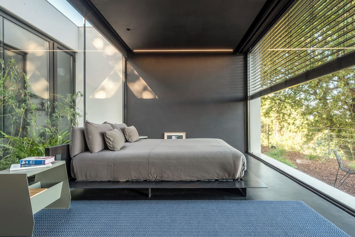 A modern bedroom with a bed, a bedside table, and a window with blinds.