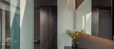 A modern bathroom with a long, dark sink, a large mirror, and a vase with flowers.