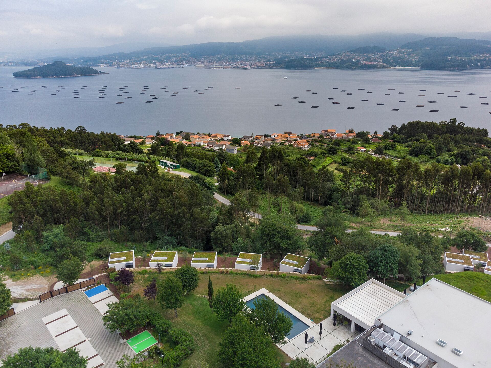 Vista aérea de uma cidade costeira com um porto de iates, edifícios residenciais e áreas verdes.