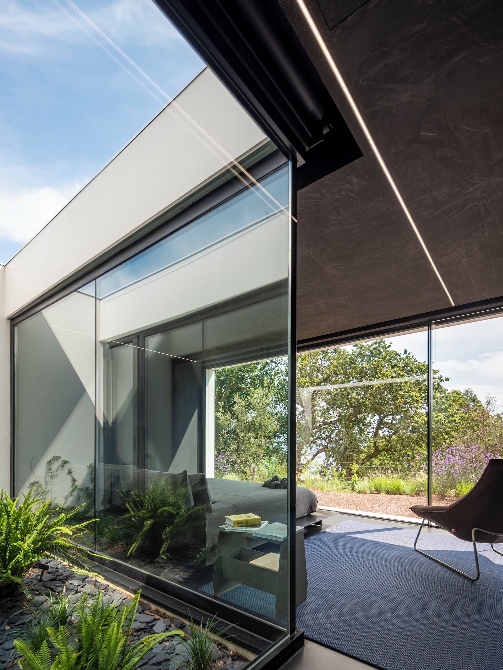 A modern interior with a glass wall, a bed with pillows, and a view of the outdoors.