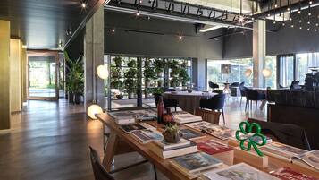 Un interior espacioso y moderno con una larga mesa mostrando libros y objetos decorativos, ventanas amplias que ofrecen luz natural y un techo alto con vigas a la vista.