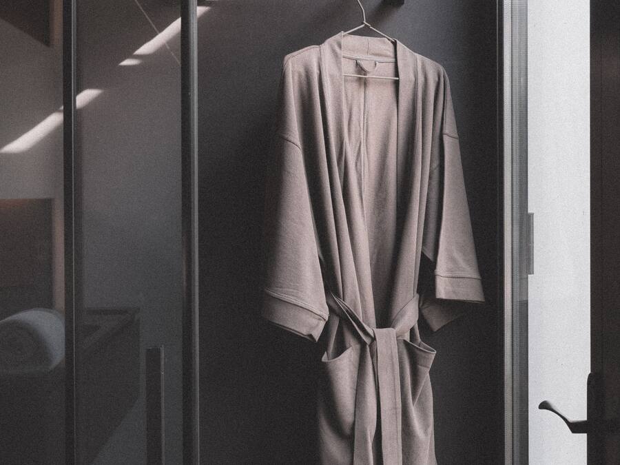 A robe hanging on a rack in a modern bathroom with a glass shower door and a towel shelf.