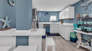 Une cuisine avec des meubles blancs, un mur bleu et une décoration sur le thème de la mer, comprenant une étoile de mer et un phare.