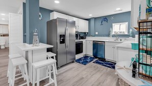 Une cuisine moderne avec un réfrigérateur en acier inoxydable, des armoires blanches et un mur d’accent bleu.