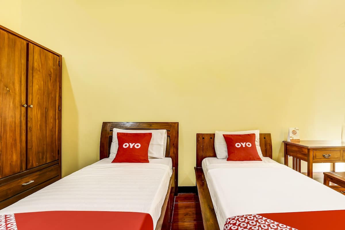 A hotel room with two single beds, each with a wooden headboard and a red pillow labeled "OYO".