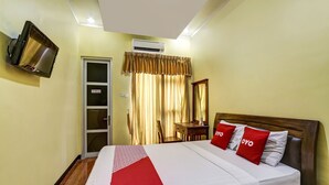 A hotel room with a bed, a TV mounted on the wall, an air conditioning unit, a wooden nightstand, and a chair. - OYO 91036 Hotel Simpang Lima Gkpri (Semarang)