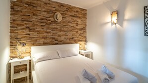 Una cama bien hecha con toallas, un muro de piedra y dos lámparas de noche en una habitación de hotel.