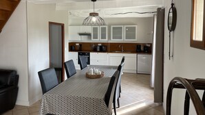 A dining area with a table set for four, a kitchen in the background, and a staircase leading to an upper level. - Gîte near Le Treport and Criel sur Mer (Saint-Martin-le-Gaillard)
