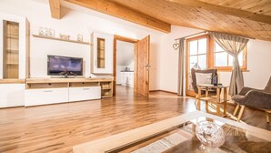 Een ruime woonkamer met een houten vloer, een flatscreen televisie, een eethoek met een tafel en stoelen, en een gezellige zithoek met een bank.