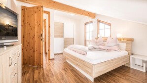 Een slaapkamer met een houten bed, een televisie en een houten garderobe.