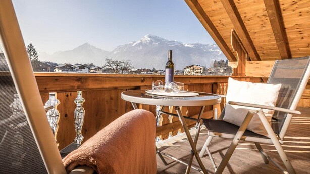 Een houten terras met een tafel, een stoel en een fles wijn.