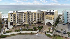 A multi-story hotel with balconies, a parking area, and a view of the ocean.