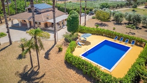 Une grande maison avec une piscine, entourée de palmiers et surplombant un ciel d’un bleu limpide.