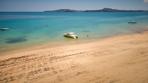 Una spiaggia con acque turchesi cristalline, una riva sabbiosa e imbarcazioni.