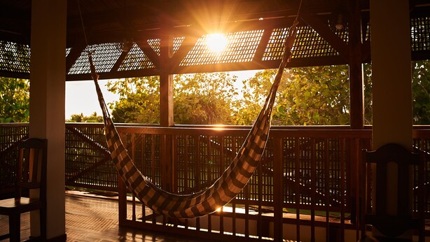 Un'amaca sotto un pergolato di legno con vista su alberi e il sole al tramonto.