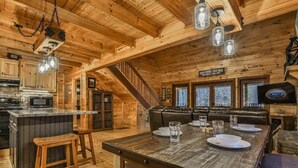 A wooden cabin interior with a kitchen, dining area, and a staircase. - Chardonnay River Chalet| Ellijay, GA (Ellijay)