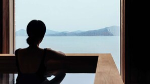 A person seated by a window overlooking a body of water with distant mountains. - IJE Namhae (Namhae)