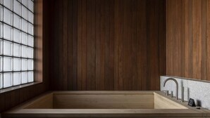 A wooden bathtub with a modern faucet, a small sink, and a glass block window. - IJE Namhae (Namhae)
