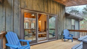 Una terraza de madera con dos sillas Adirondack, un vidrio que da a un espacio interior y una barandilla de madera.