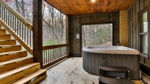 Terraza de madera con jacuzzi, una escalera y vistas a árboles.