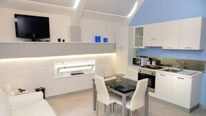 Una cucina moderna con mobili bianchi, un tavolo da pranzo con sedie, una TV integrata e una finestra con persiane.