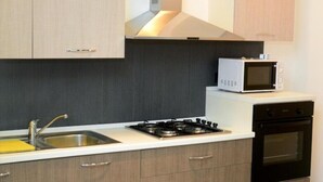 Una cocina moderna con armarios de madera clara, un lavamanos de acero inoxidable, una estufa a gas, un microondas y un horno empotrado.