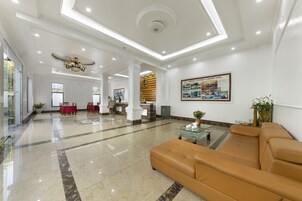 Um hall amplo com piso de mármore, um sofá de couro marrom, uma mesa de centro de vidro e um balcão de recepção.
