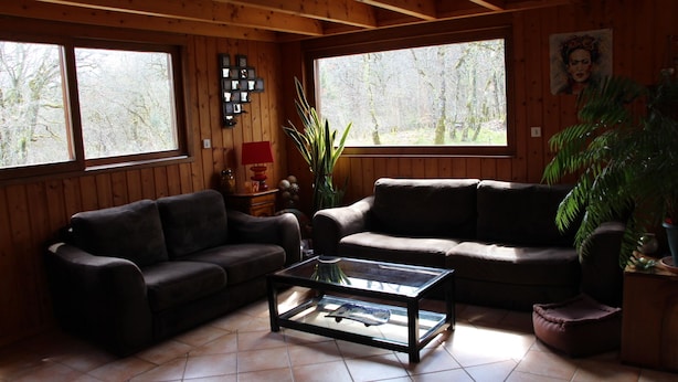 Una sala de estar acogedora con dos sofás, una mesa de centro de vidrio y grandes ventanales con vistas a árboles.