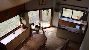 Una cocina con armarios de madera, una mesa de comedor y sillas. Hay plantas en macetas en el alféizar de la ventana y una ventana con vistas al exterior.