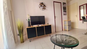 A living room with a TV on a wooden stand, a glass table, and a potted plant. - Holiday home near the beach (Cap d'Agde)