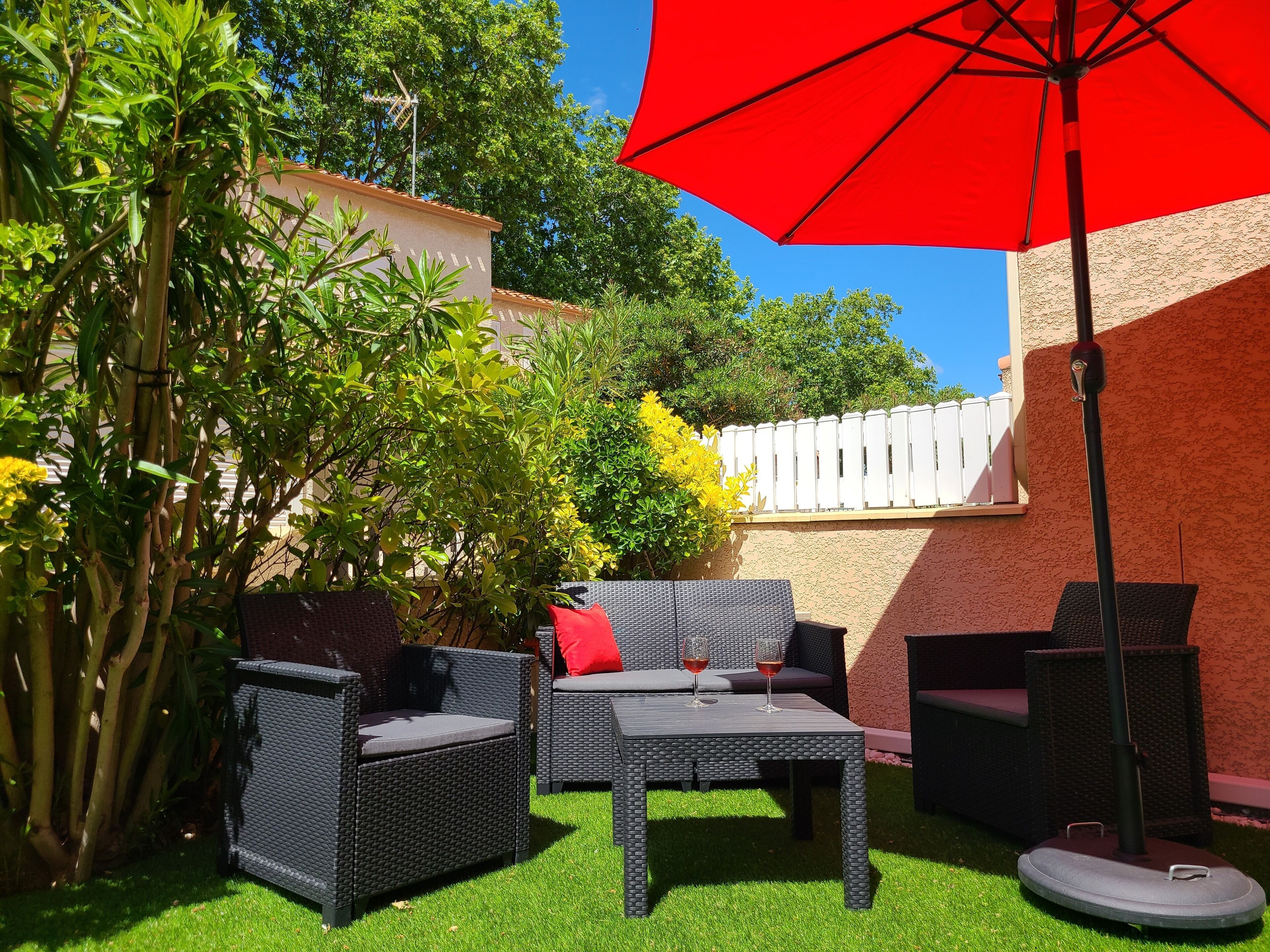 An outdoor patio area with wicker furniture, a red umbrella, and green artificial grass.